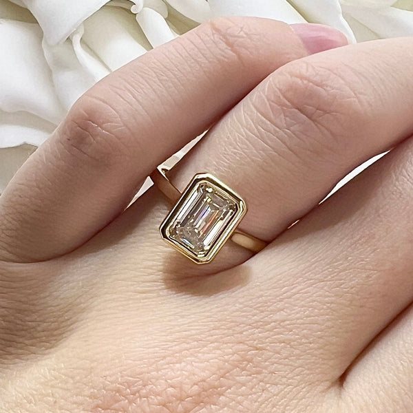 Gold ring with a large diamond on a hand against a white fabric background