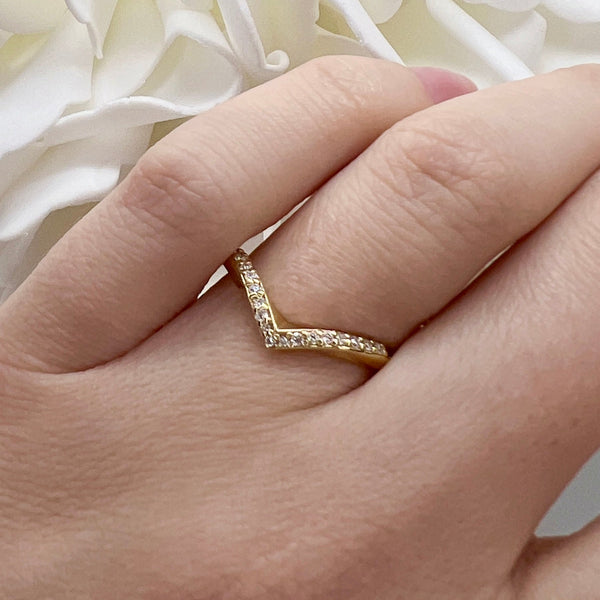 Gold ring with a chevron design on a hand against a white floral background