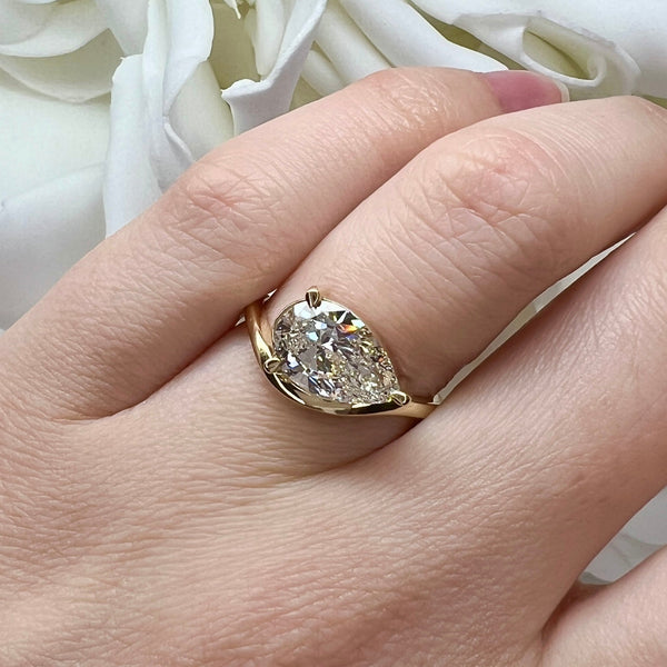 Gold ring with a large diamond on a hand against a white floral background
